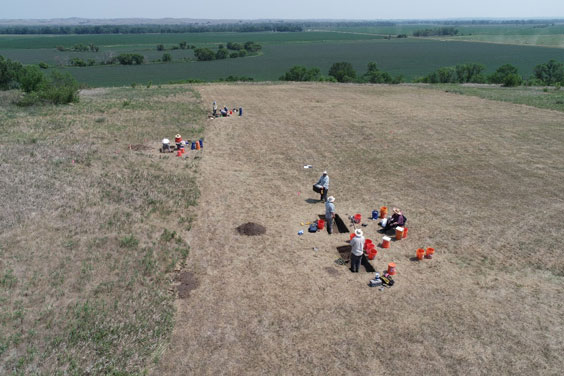 Many people can be seen working on a piece of land with many orange buckets by them
