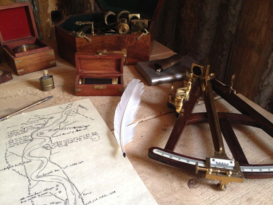 Many tools, including a map, quill, ink, an other items used to make maps, sit atop a desk.