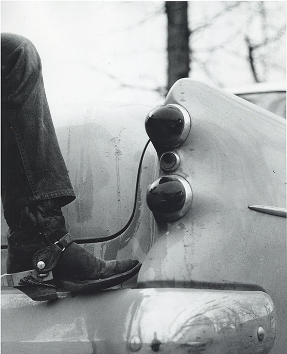 BW vintage photo of a jean clad leg and boot on a car bumper