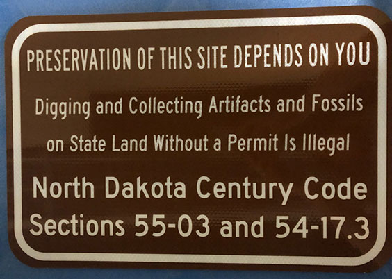Sign that reads the following: Preservation of this site depends on you. Digging and collecting artifacts and fossils on state land without permit is illegal. North Dakota Century Code Sections 55-03 and 54-17.3