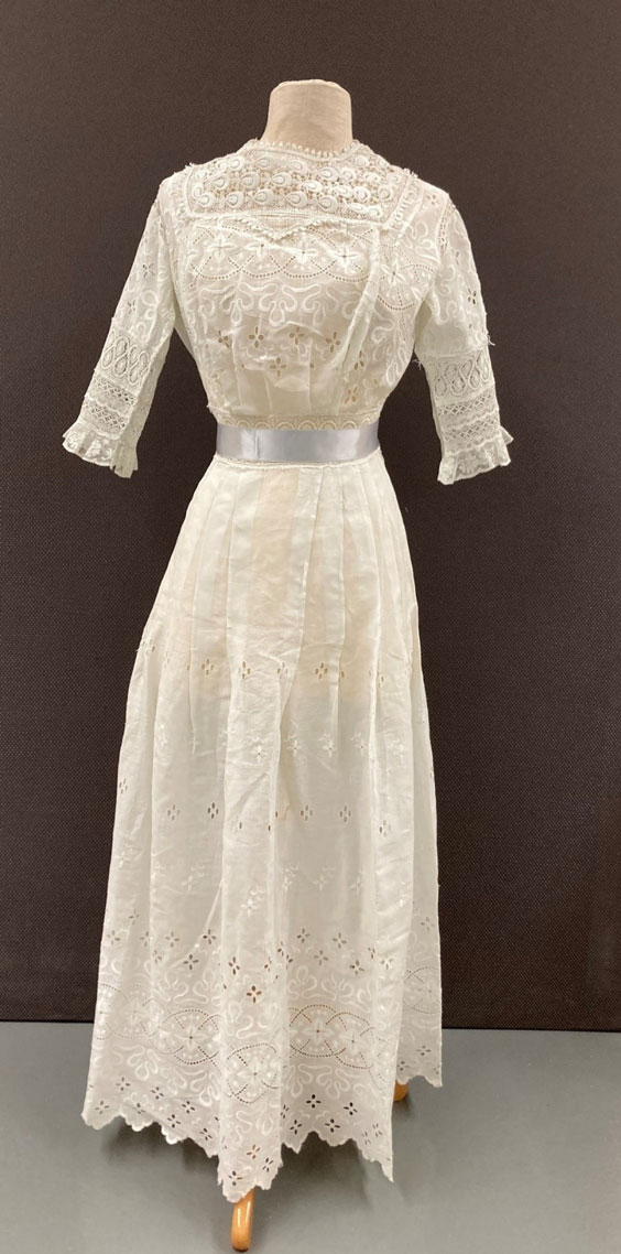 White dress on a mannequin with a silver ribbon around the waist. There are floral pattern cutouts throughout the dress.