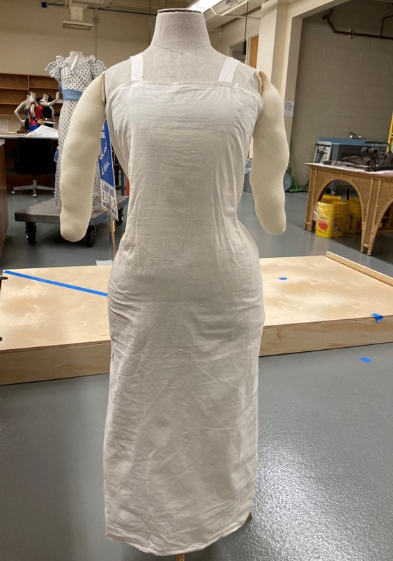 A headles mannequin with a full-length cotton slip over it and stuffed arms attached