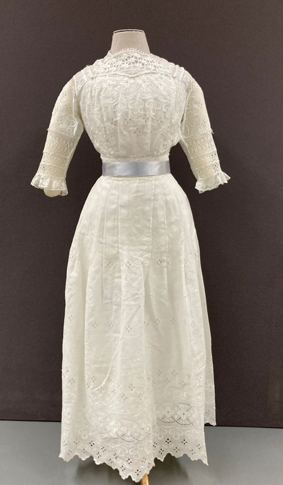 White dress on a mannequin with a silver ribbon around the waist. There are floral pattern cutouts throughout the dress.