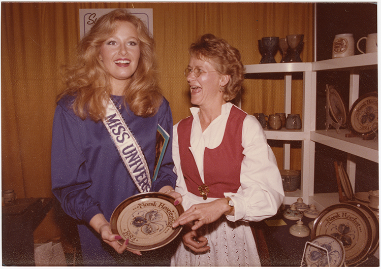 Miss Universe 1984 poses with a Norsk Høstfest vendor holding a commemorative plate with a Scandinavian design. SHSND SA 11762
