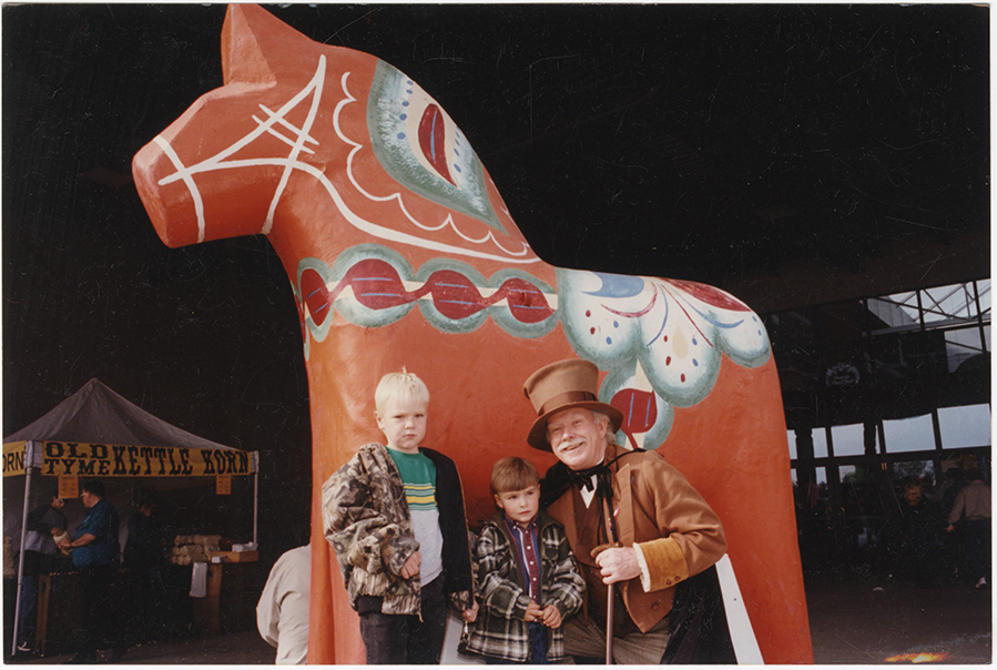 This man, dressed as Danish author Hans Christian Andersen, poses with two children in front of the beloved Norsk Høstfest Dala horse, 2001. SHSND SA 11762
