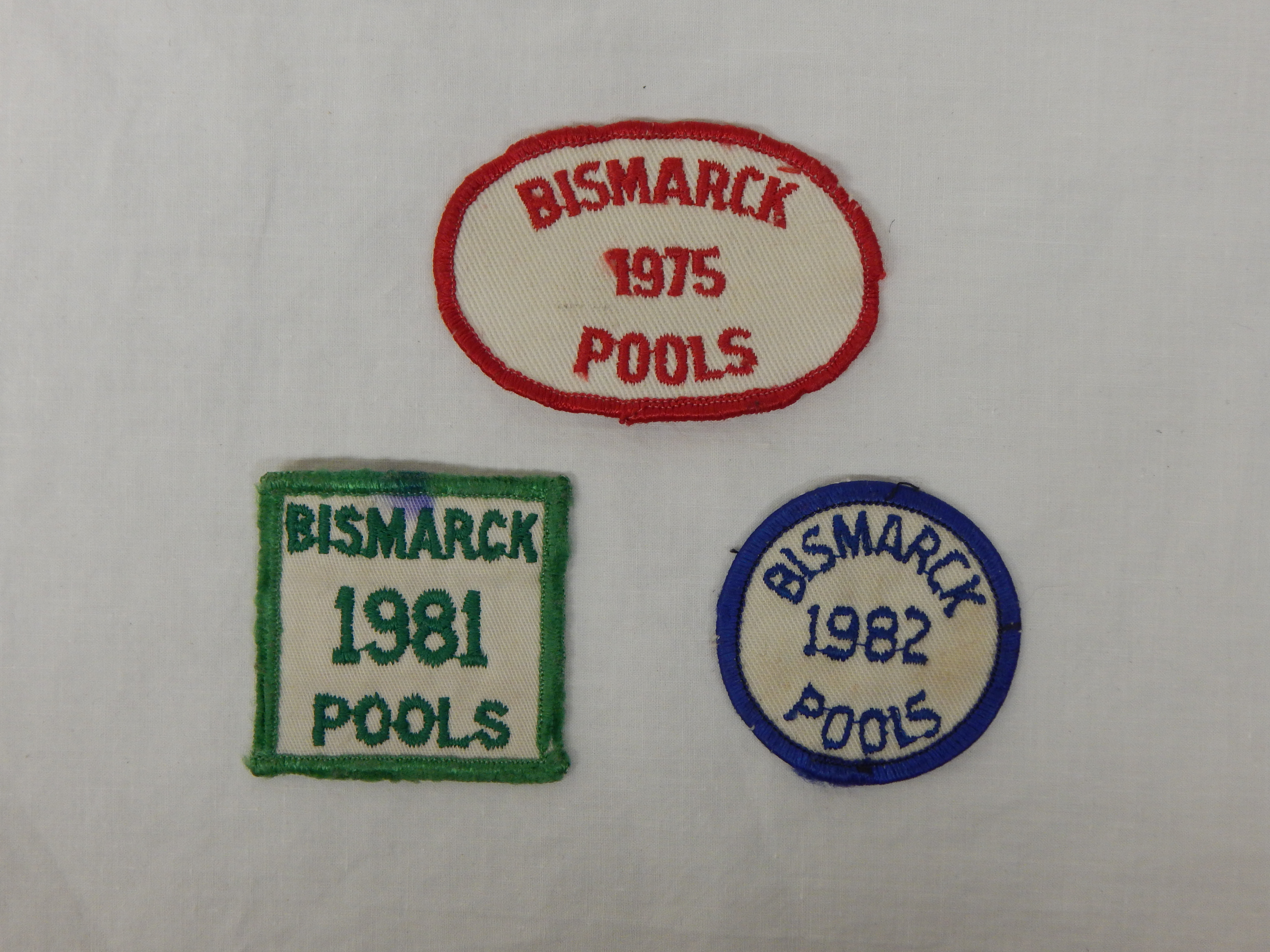 Bismarck Pools annual pass patches for 1975, 1981, and 1982 used by the children of Joseph F. Schneider and Vera Wahlman. SHSND 2018.86.1-3
