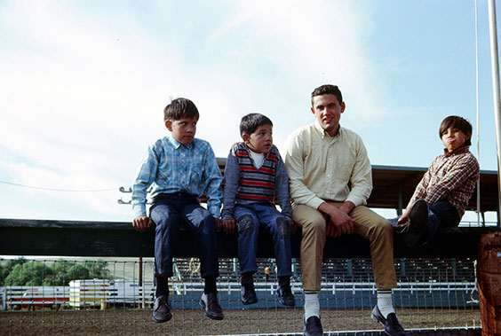 Four boys sitting on fence at rodeo