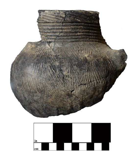 A dark brown piece of broken pottery with horizontal lines at the top and angled lines throughout the rest of it.