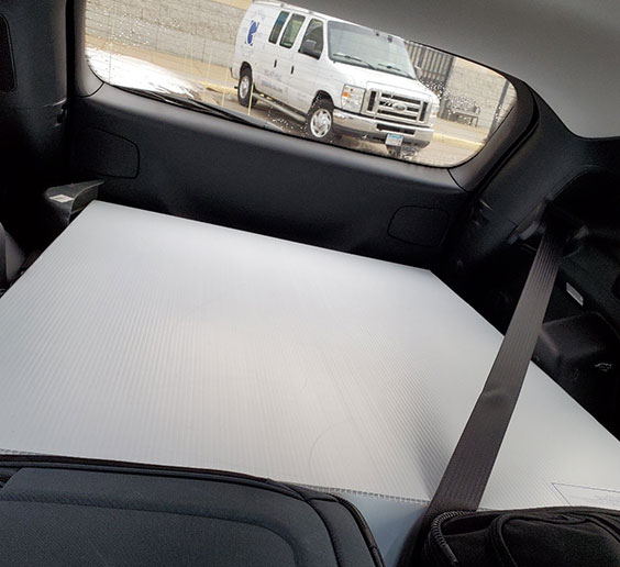 The inside back of a vehicle with a white box loaded in it. A white van can be seen through the back window.