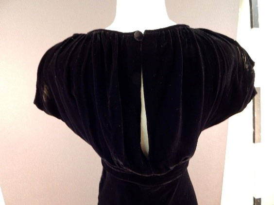 The back of a black velvet dress. It shows an opening going down the middle of it to just above the waist.