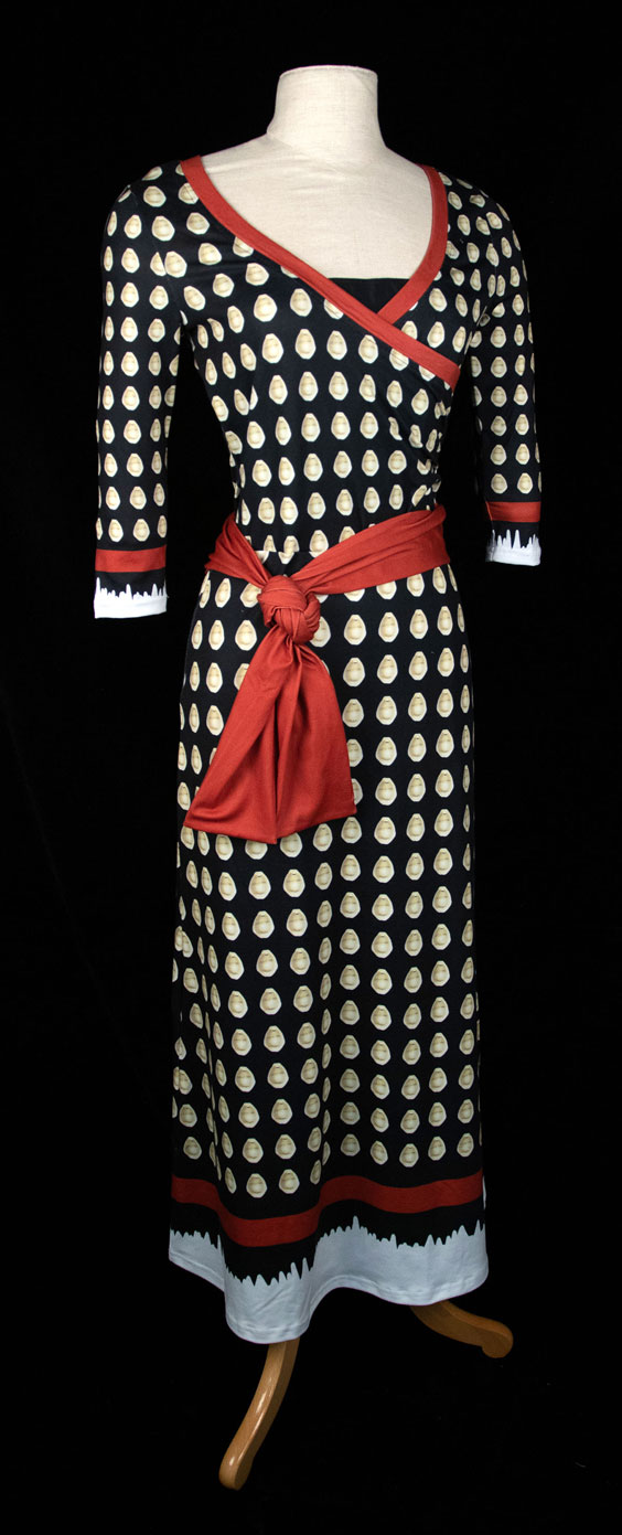 A black dress with red trim and a red tie around the wais. On the black fabric is the backside of cowrie shells repeated throughout.