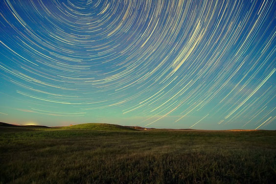 A grassy field is shown with swirls of light in the sky.