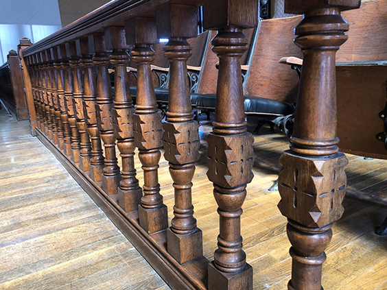 Railing banisters are shown with a more square shape in the middle and a cross shape carved into it. Above and below the square shape, the banisters are more cyllindrical with wider and narrower parts and rings 