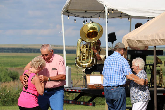 Two couples dance outdoors in front of a tent with a tuba player and piano player.