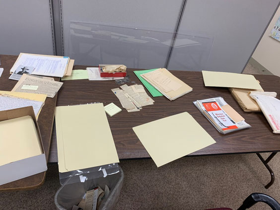 A table is shown with folders, papers, and images scattered on it.