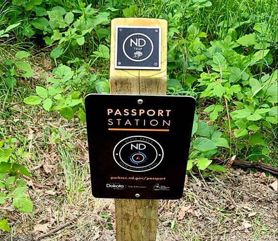 A wooden post with an ND TRSP plaque hung on the top and a Passport Station sign hung on the front