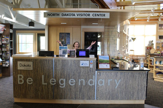 A woman stands holding her arms up and apart and is behind a big desk that says Be Legendary