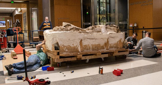 Four men are gathered around working on a large plaster block containing dinosaur fossils 