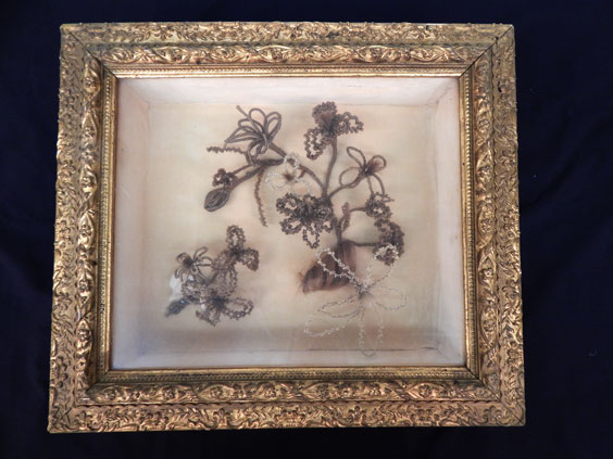 A framed case that displays flower art made out of hair