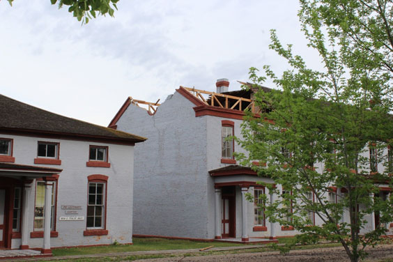 A white building with red trim around the windows and roof is shown with part of the roof blown off
