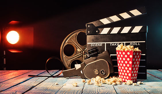 A video reel, camera, action marker, and tub of popcorn sit on a wooden floor with a spotlight shining on them