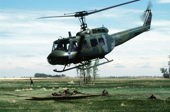 A green camo helicopter hovers just above the ground