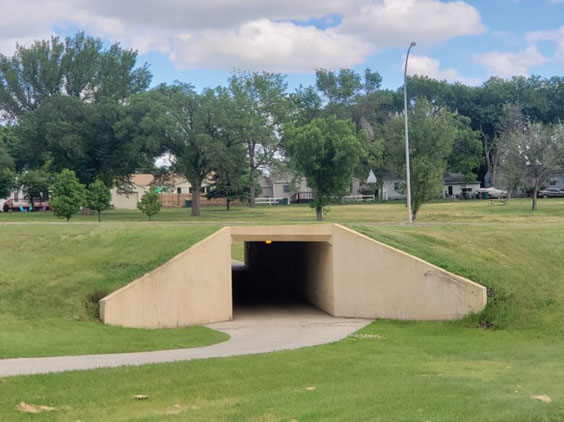 A walking tunnel under a road is shown with a sidewalk leading up to it