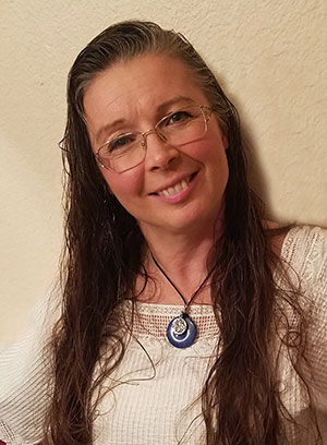 A middle-aged woman with long, dark hair and wire framed glasses smiles for the camera