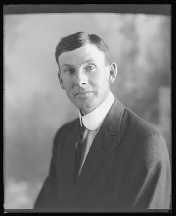 A young man with short dark hair sits posing for the cameran in a white collared shirt, dark colored tie, and dark colored suit jacket.