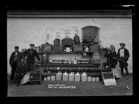 Five men stand outside around many bottles and jugs of varying sizes.