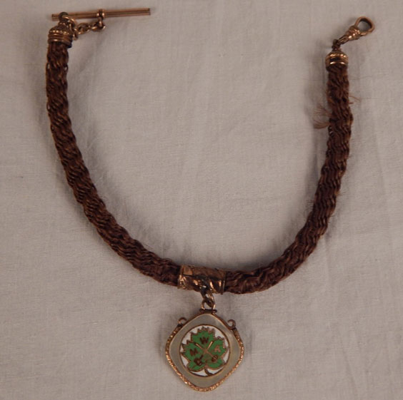 A braided necklace made of dark hair hair with a leaf charm hanging from the middle.