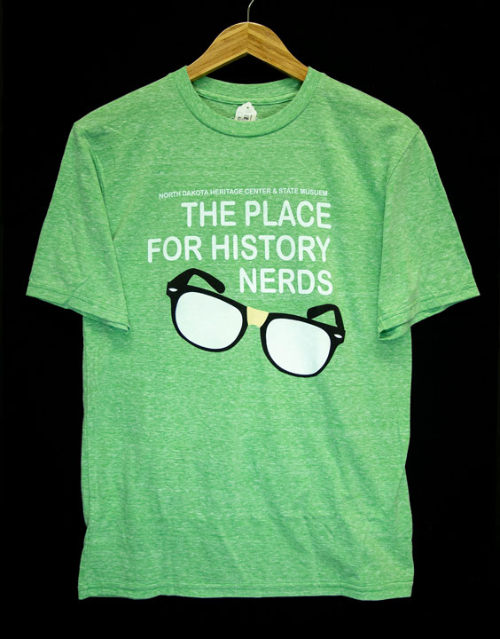A green t-shirt that reads North Dakota Heritage Center & State Museum - The Place for History Nerds with a pair of black rimmed glasses with tape in the middle below the text
