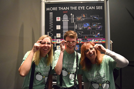 Three women dressed as nerds look as if they're having troubles seeing as they stand in front of a sign that reads More Than the Eye Can See