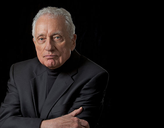 an older man takes a portrait photo in a black suit with a black background