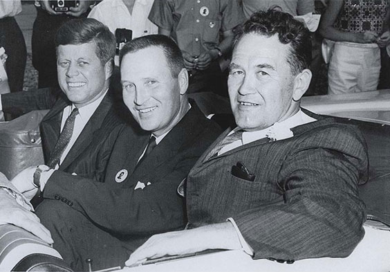 President John F. Kennedy, William Guy, an Quentin Burdick, all wearing suits and ties, are shown smiling as they look towards the person taking the photo