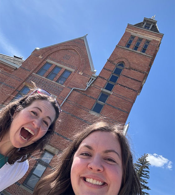 Two dark haired women taking a selfie in front of an old brick building