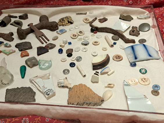 Many artifacts including buttons, pottery, etc. sit on a tan cloth in a tray