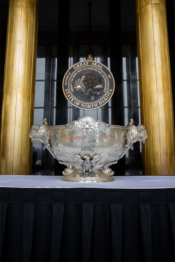 The USS North Dakota Silver Service punch bowl sits on a table in front of the State Seal.