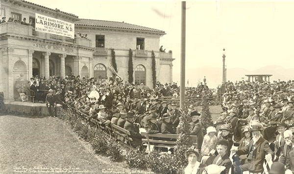A group of people is gathered outside a building with a banner hanging from it that reads Have a baked potato on us. Larimore, N.D. The best potatoes grown in the best potato country on earth.