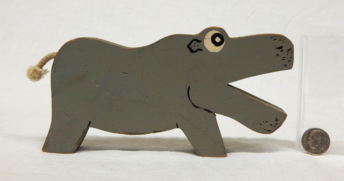 A gray male hippo made of wood with its mouth open. Its tail is made of rope.