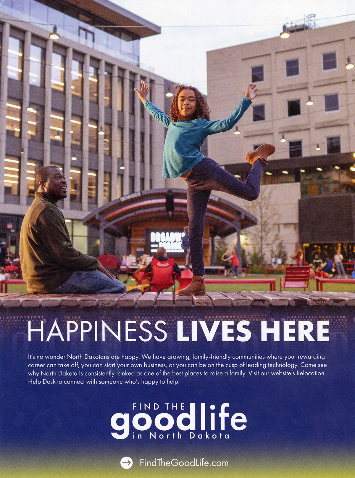 Advertisement that reads Happiness Lives Here. It's no wonder North Dakotans are happy. We have growing family-friendly communities where your rewarding career can take off, you can start your own business, or you can be on the cusp of leading technology. Come see why North Dakota is consistently ranked as one of the best places to raise a family. Visit our website's Relocation Help Desk to connect with someone who's happy to help. Find the goodlife in North Dakota. FindTheGoodLive.com. Shown on the ad are a young girl dancing while a man smiles at her. There's a stage in the background with people seated and standing on a lawn with buildings around the lawn.