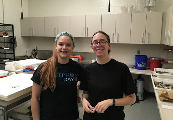 Two women standing in a room with table and cabinets