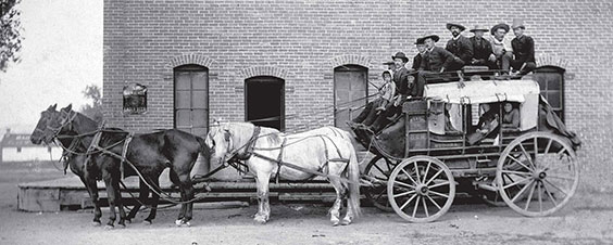 black and white photo of a horse drawn wagon with mail and people on top
