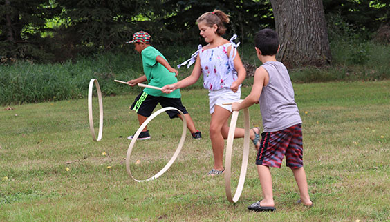 Three kids roll hoops with sticks