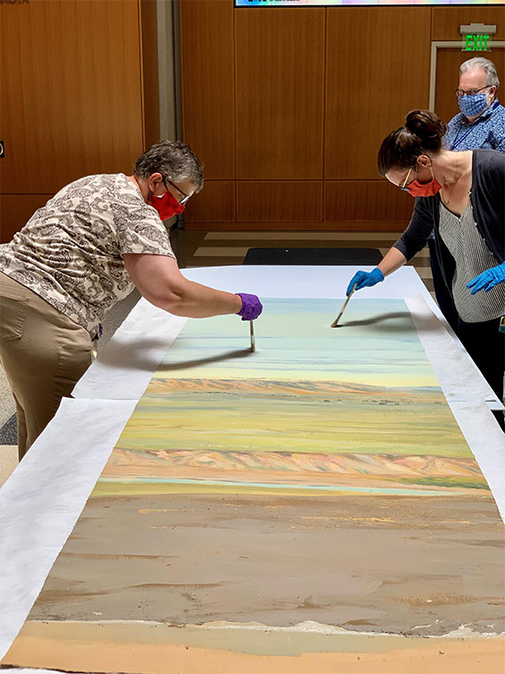 museum staff carefully brushing loose particles from mural pieces