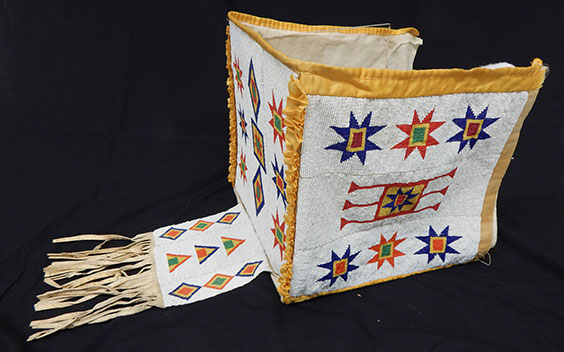 A beaded cradle hood with yellow trim. The main area is beaded in white and there are red stars with yellow and red squares inside them, red squared with yellow and green quares inside, and triangle, diamond, and square shapes in the same colors.