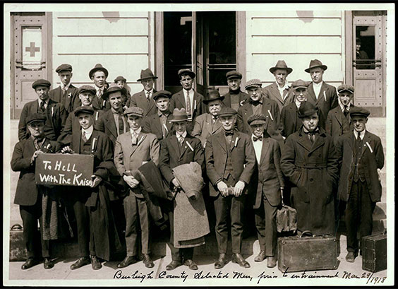 Men standing outside building. Two men hold a sign together that says To Hell With The Kaiser