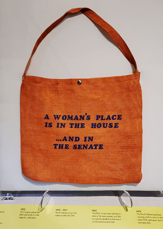 orange burlap tote bag reading “A woman’s place is in the House . . . and in the Senate.”