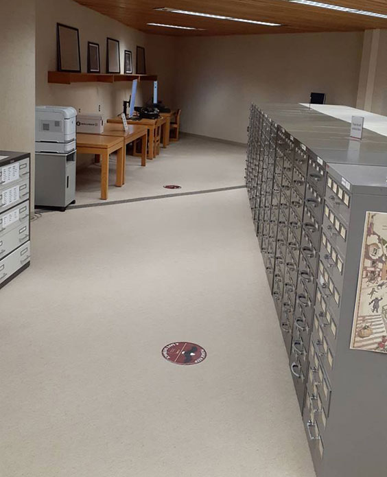 A row of gray filing cabinets line the right side and tables with computers, printers and scanners line the left side.