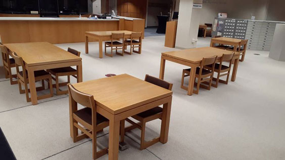Two square wood tables with two chairs each and three rectangle wood tables with two to three chairs are shown spaced apart for social distancing.
